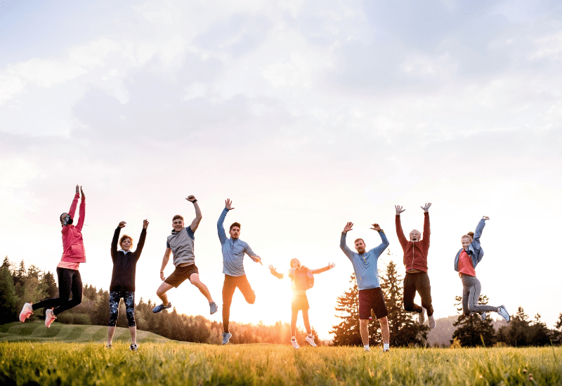 A group of people leaping into the air with their arms raised in a field at sunset