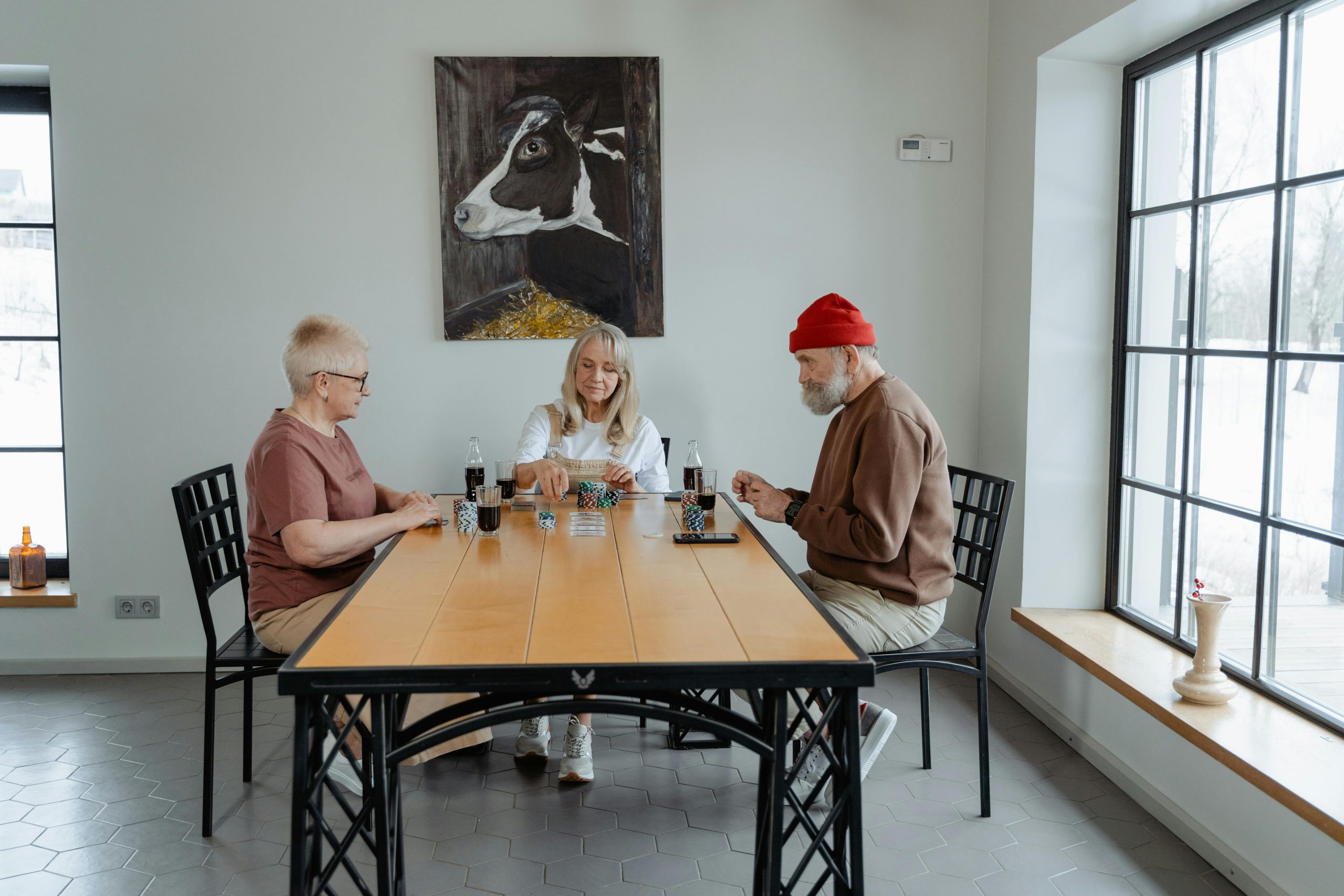 Three people sitting around a long dining table in a bright room with tall windows
